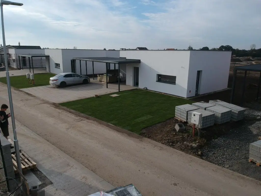 Široký pohľad na jednopodlažný objekt, trávnik a spevnené plochy